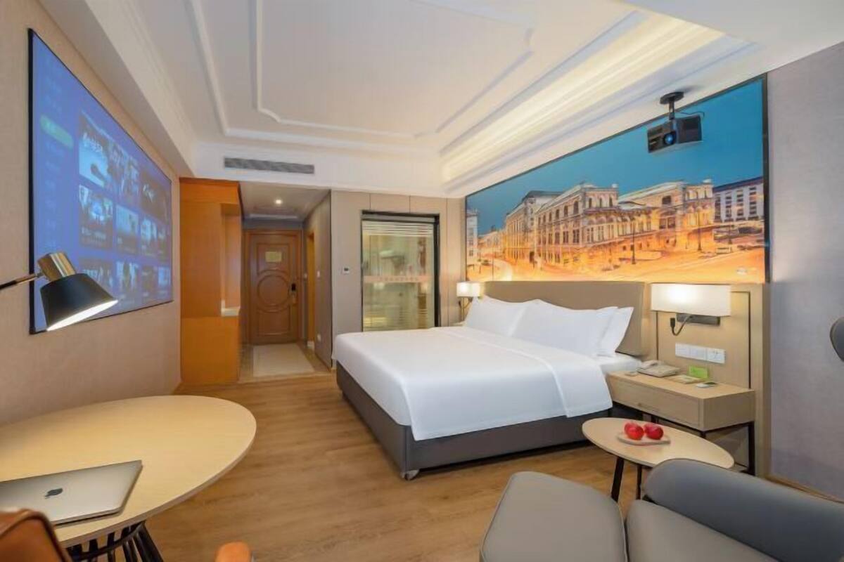 Une chambre d’hôtel équipée d’un lit, d’un bureau, d’une chaise, d’une petite table et d’un écran de projection.