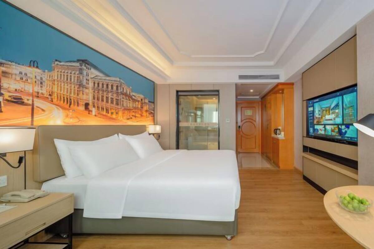Une chambre d’hôtel avec un lit, une table de chevet, une lampe et un téléviseur fixé au mur.