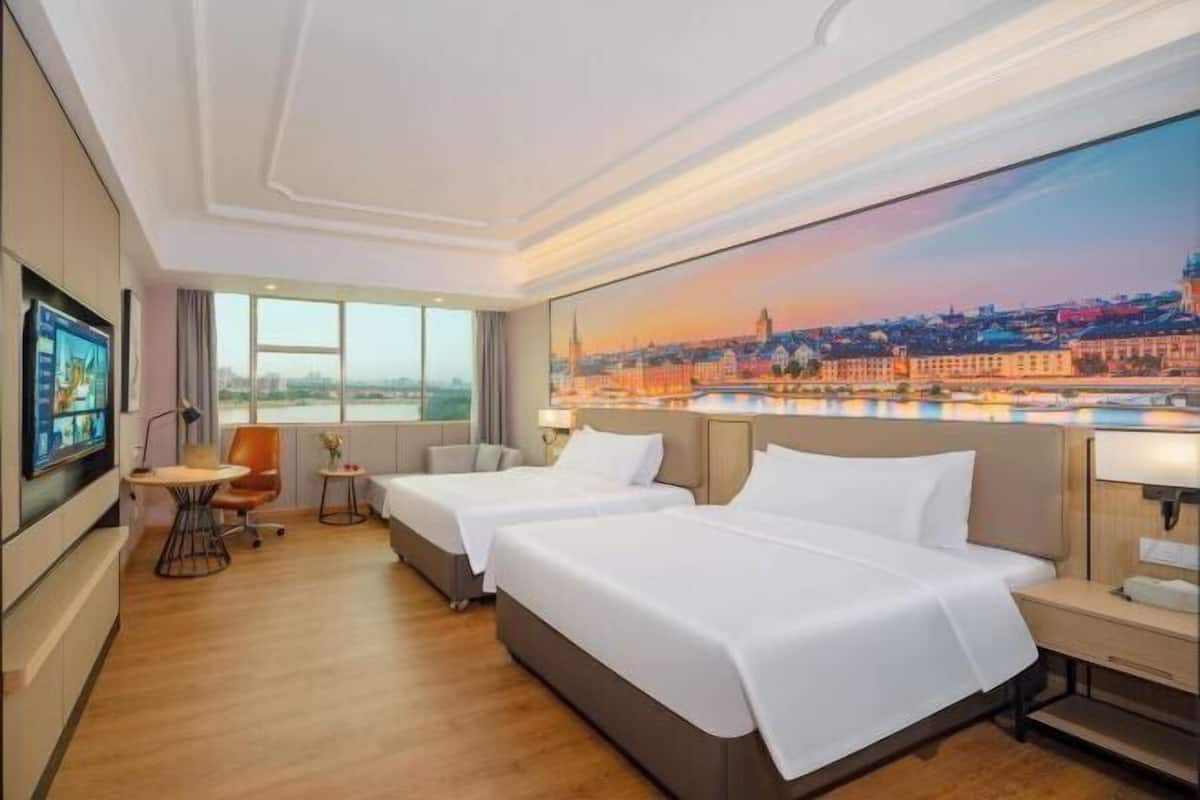 Une chambre d’hôtel avec deux lits, une télévision, une petite table et un tableau représentant un paysage urbain.