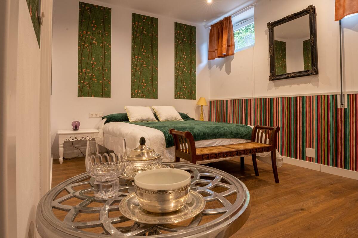 A room with a bed, a table with a decorative centerpiece, a mirror, and a striped wall.