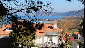 A building with a red roof and white walls, surrounded by trees and a view of the sea and mountains. - finca dos mares  (Ferrol)