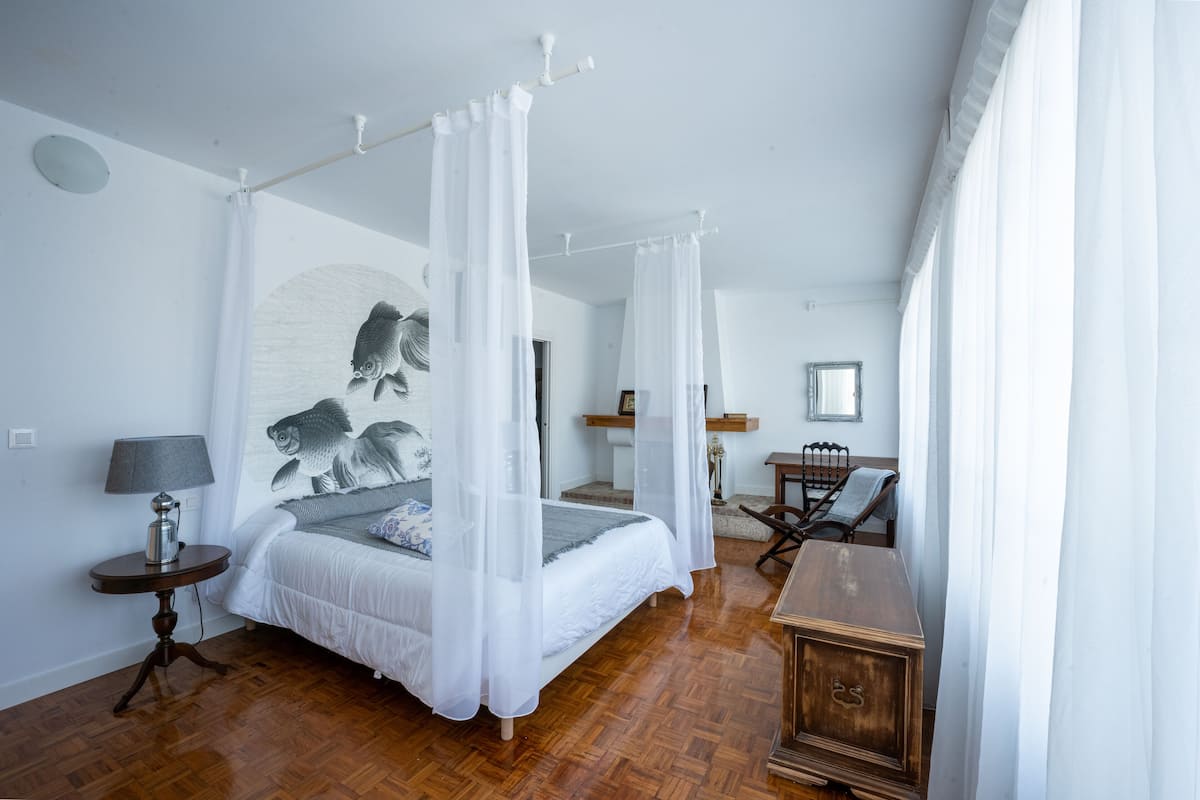 A bedroom with a four-poster bed, a bedside table with a lamp, a wooden dresser, and a large fish mural on the wall.