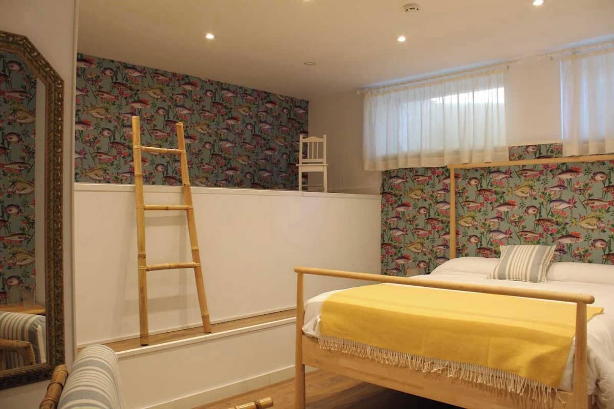 A bedroom with a bed, a ladder, a window with curtains, and a wall with a fish pattern.