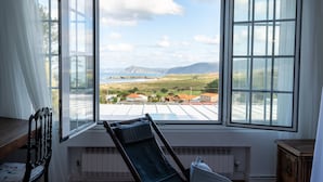 A room with a large window offering a view of a landscape with mountains and buildings. - finca dos mares  (Ferrol)