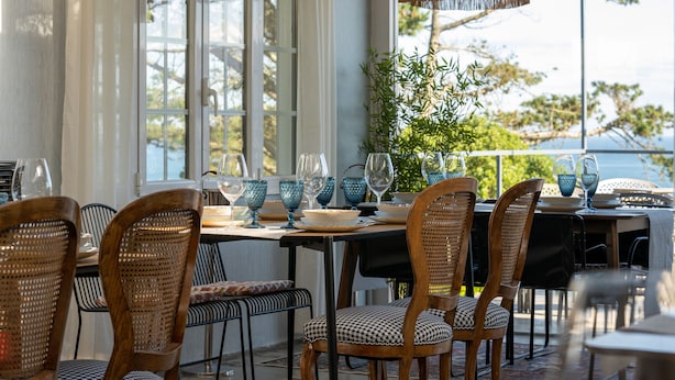 An outdoor dining area with wicker chairs, a table set with blue glassware, and a view of the sea. - finca dos mares  (Ferrol)