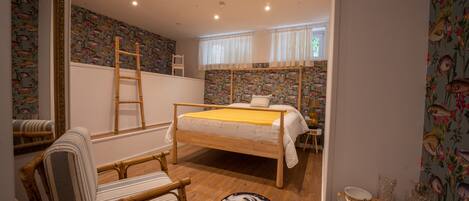 A room with a bed, a chair, a ladder, and a table with dishes.