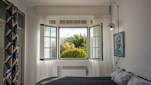 A bedroom with a large window, a radiator, a bed with patterned bedding, and a wall-mounted light fixture. - finca dos mares  (Ferrol)
