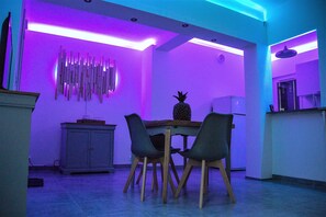 Un comedor con una mesa y sillas de madera, una piña sobre la mesa, y una pared con listones de madera verticales.