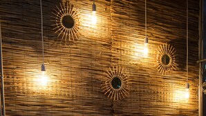 Ein Zimmer mit gewebter Wand, hängenden Lampen, einem Tisch mit Kerze, Weinflaschen und Gläsern.