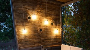 Eine Terrasse im Freien mit Holzboden, weiß gepolsterten Sitzgelegenheiten und hängenden Lampen.