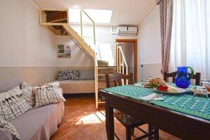 A cozy living room with a sofa, a dining table set with food, a staircase, and a window with curtains. - "Case Cosi" Suite with Terrace Castel Sant'Elmo (NAPOLI)