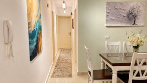 A hallway leading to a dining area with a table and chairs, a painting on the wall, and a telephone on the wall. - Casa De Elegant (New Cairo)