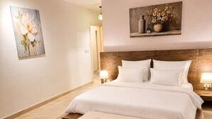 Hotellihuone, jossa on suuri sänky, puinen pääty, yöpöytä lampun kanssa ja taulu seinällä.