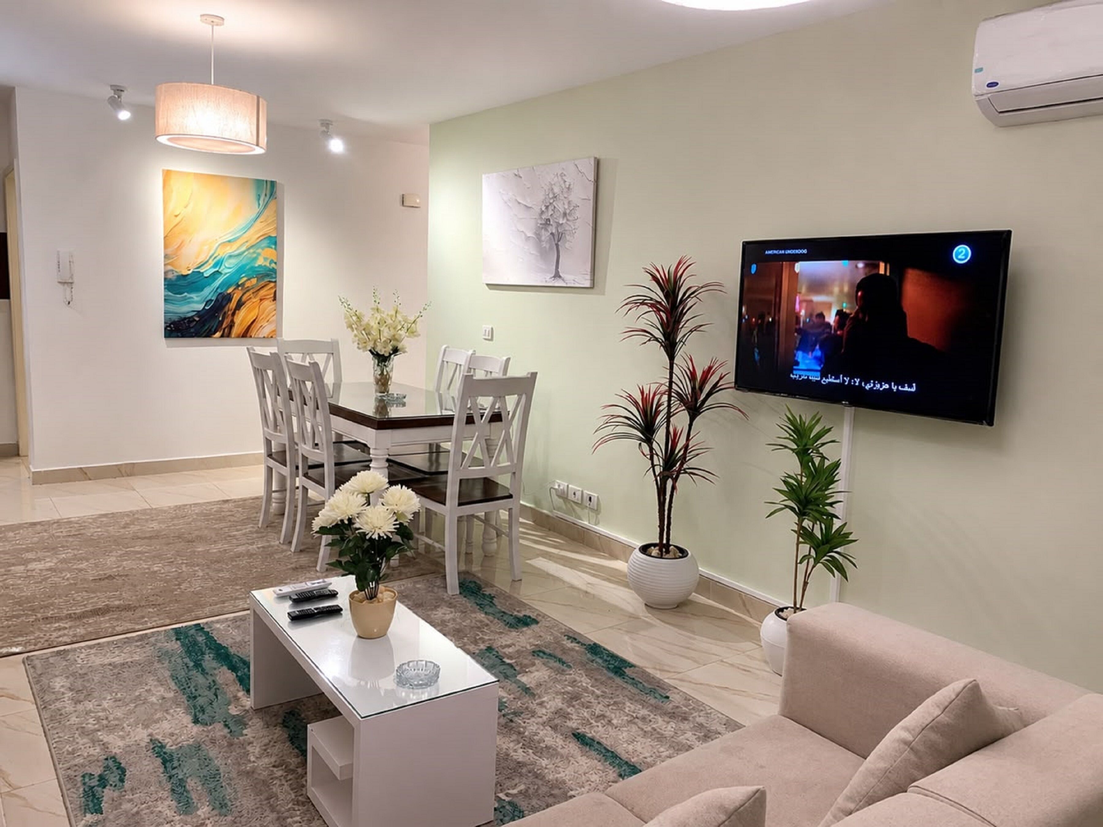 Een moderne woonkamer met een flatscreen televisie, een eethoek en decoratieve planten.
