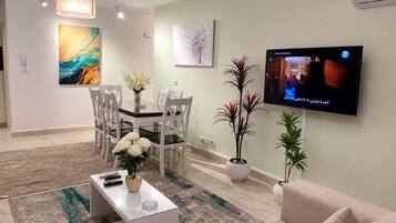 Een moderne woonkamer met een flatscreen televisie, een eethoek en decoratieve planten.