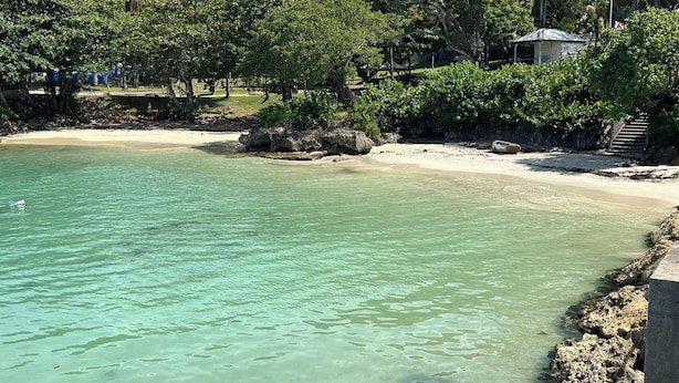 A beach with clear turquoise water, a sandy shore, and a rocky outcrop.