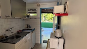 A compact kitchen with a sink, stove, and a coffee maker. A window provides natural light, and there's a door leading outside.