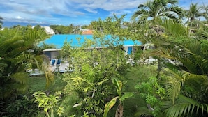 A tropical resort with a pool, lush greenery, and a clear blue sky.