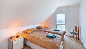 A bedroom with two beds, a nightstand, a chair, and a window.