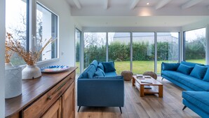 A modern living room with a blue sofa set, wooden coffee table, and a view of a garden through large windows.