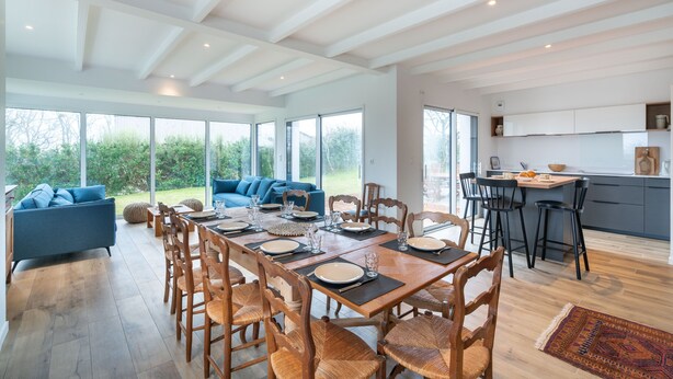 A spacious dining area with a long wooden table set for six, surrounded by wooden chairs with woven seats.