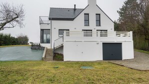 A modern two-story house with a balcony, a garage, and a swimming pool in the background.