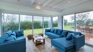 A modern living room with two sofas, a coffee table, and large windows offering a view of the garden.