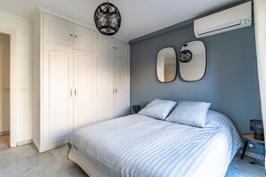 Una camera da letto con un letto, un'armadio bianco, due specchi a parete e un condizionatore d'aria.
