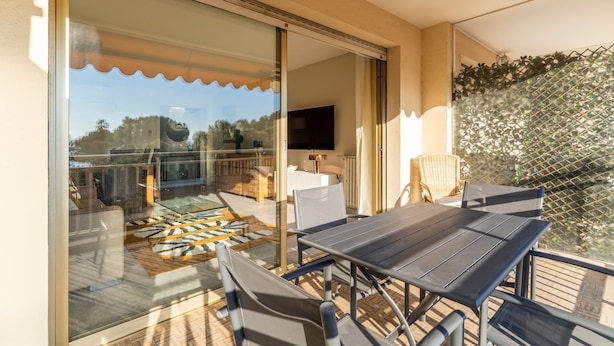 Un balcon avec une porte-fenêtre, du mobilier d’extérieur et un téléviseur en arrière-plan.