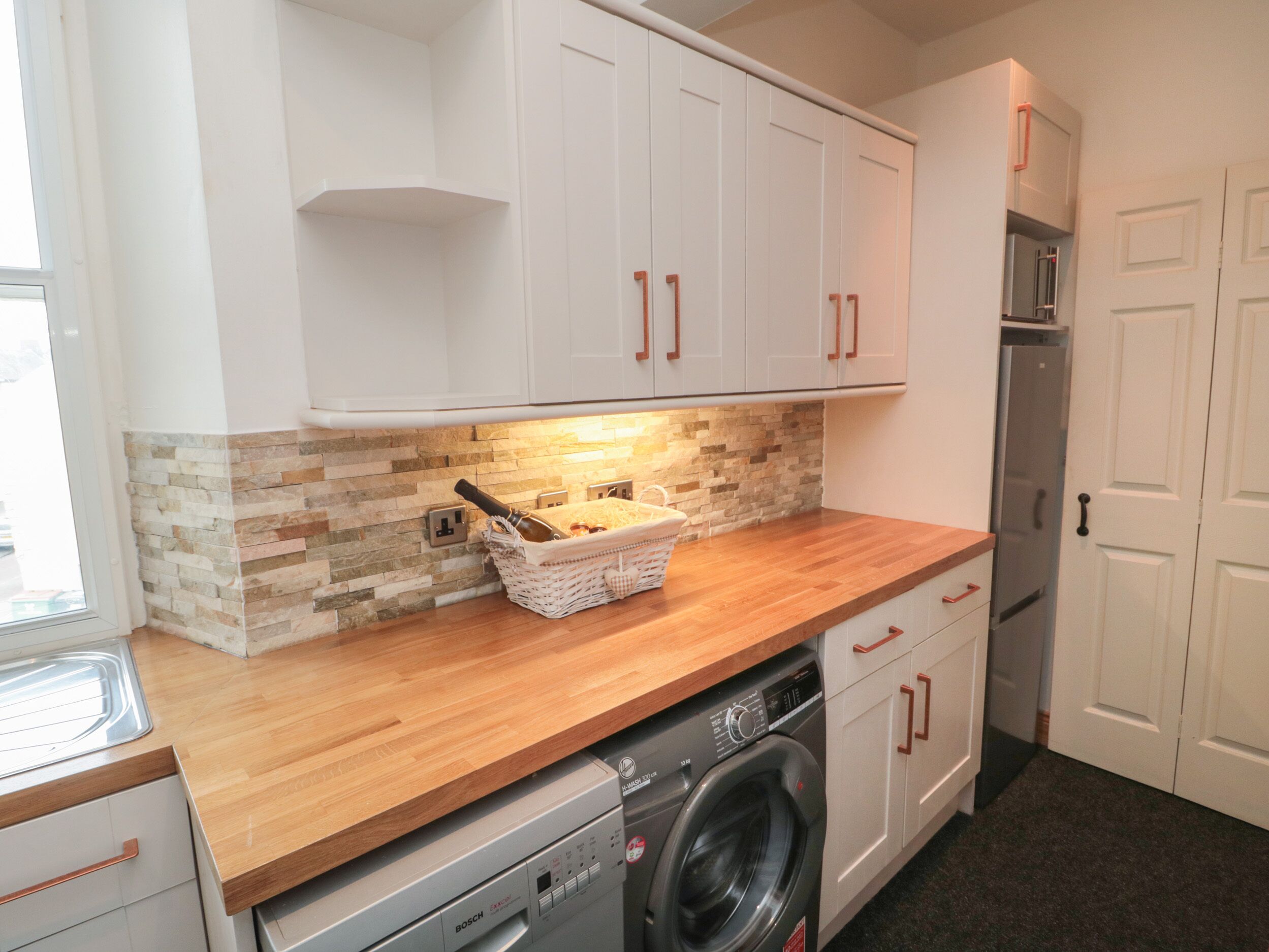 Una cocina compacta con armarios blancos, encimera de madera, lavadora y salpicadero de azulejos.