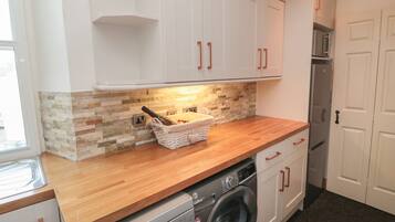 Una cocina compacta con armarios blancos, encimera de madera, lavadora y salpicadero de azulejos.