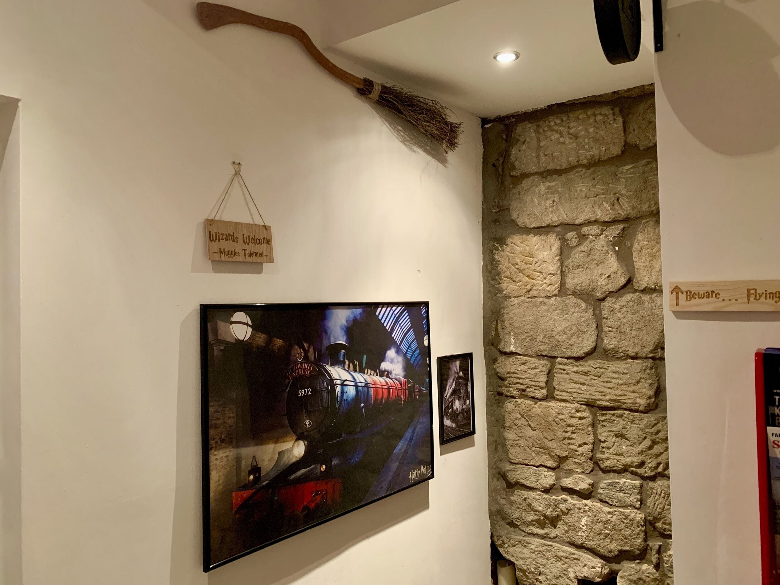 A wall with a sign reading "Wizards Welcome - Muggles Tolerated" and a framed picture of a train.