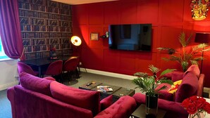 Un soggiorno con una parete rossa, una libreria, una TV a schermo piatto, un divano e un tavolino da caffè.