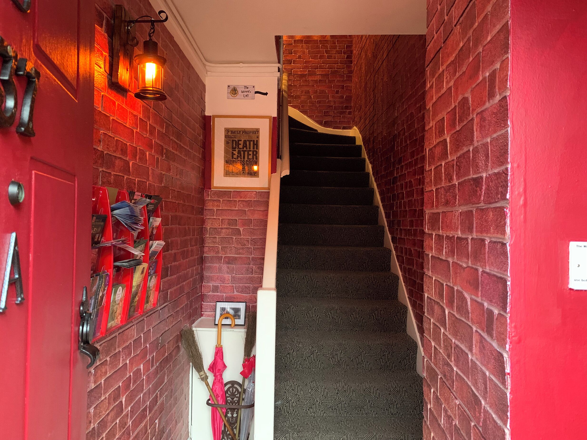 A narrow hallway with red brick walls, a red door, and a staircase leading to an upper floor.