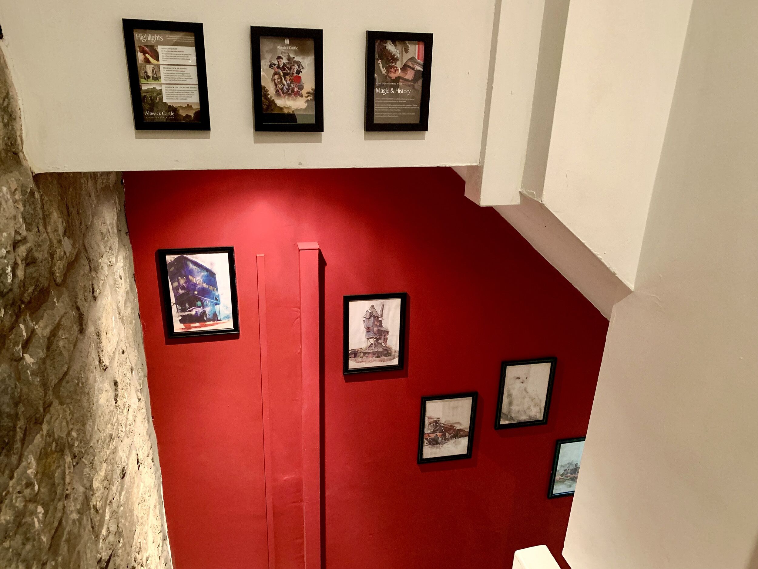 Una galería con cuadros enmarcados en una pared roja, incluyendo un autobús de dos pisos y un castillo.