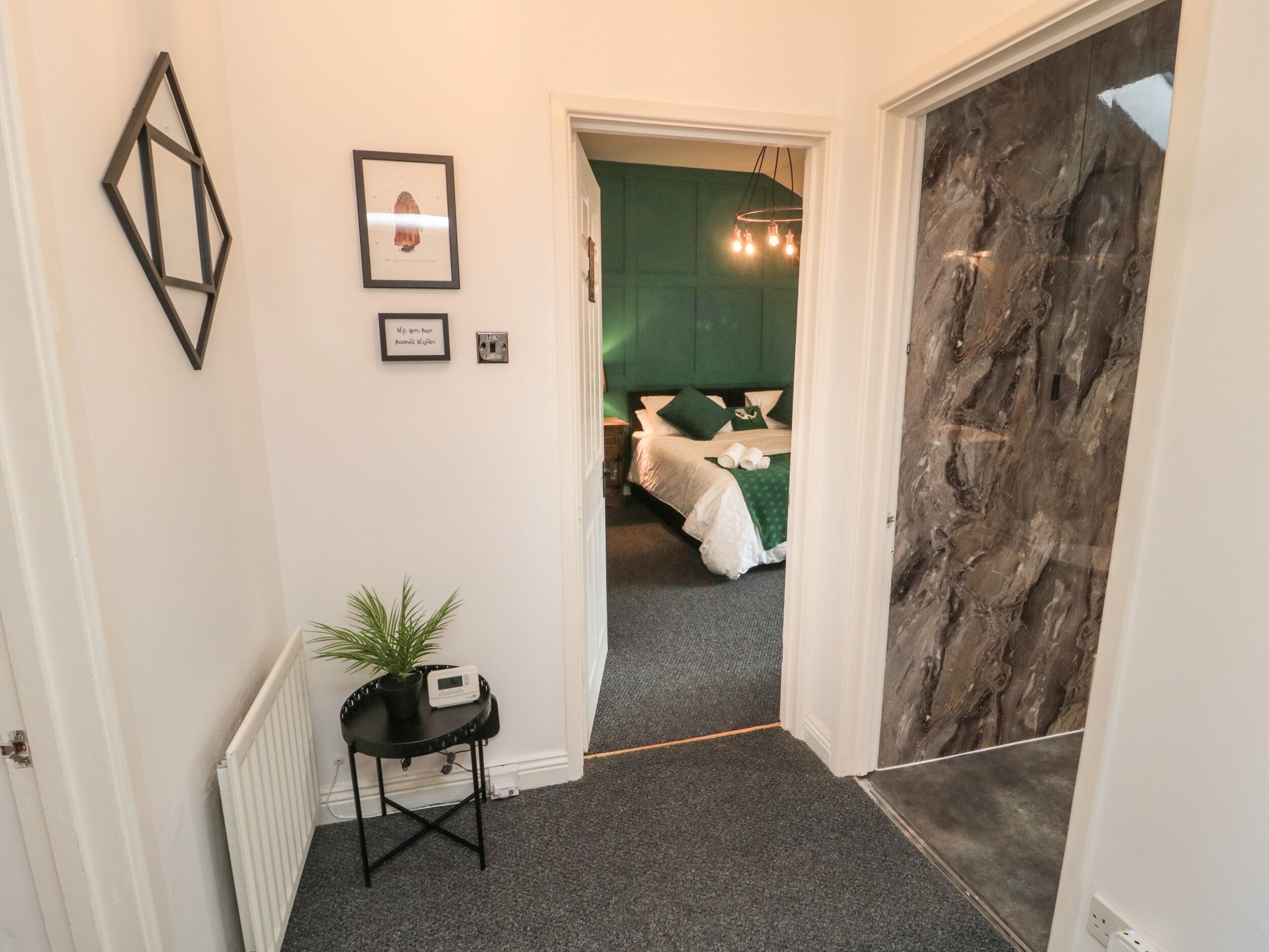 A hallway leading to a bedroom with a green wall, a bed with white linens, and a small table with a plant.