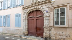 Ein Gebäude mit einer großen, braunen Doppeltür, einem steinernen Bogen und einem Fenster mit Rollläden.