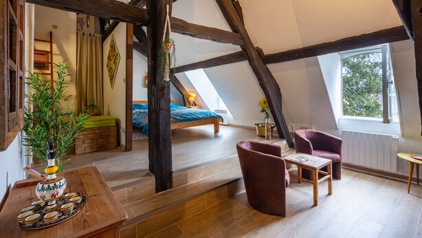 Ein gemütliches Schlafzimmer im Dachgeschoss mit freiliegenden Holzbalken, einem Bett, einem Schreibtisch und einem Sessel.