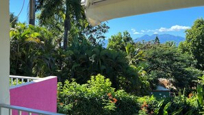 A balcony with a view of lush greenery and mountains in the distance.