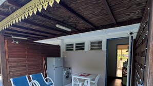 A covered outdoor area with a table and chairs, a washing machine, and a refrigerator.