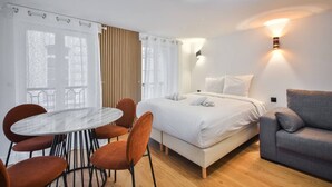 A modern hotel room with a bed, a dining table with chairs, a sofa, and a wall-mounted light fixture. - 33.Studio 4Pers#Madeleine#Gallerie La Fayette (Paris)