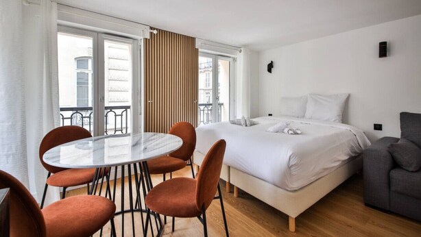 A modern hotel room with a bed, a dining table with chairs, and a balcony with a view of the city. - 33.Studio 4Pers#Madeleine#Gallerie La Fayette (Paris)