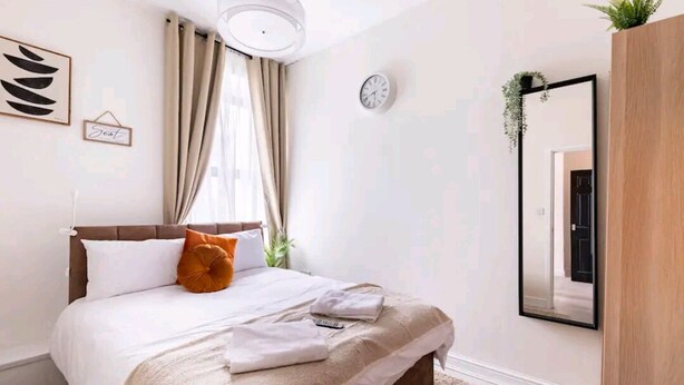 Ein Schlafzimmer mit einem Bett, einer Uhr, einem Spiegel und einer Pflanze.