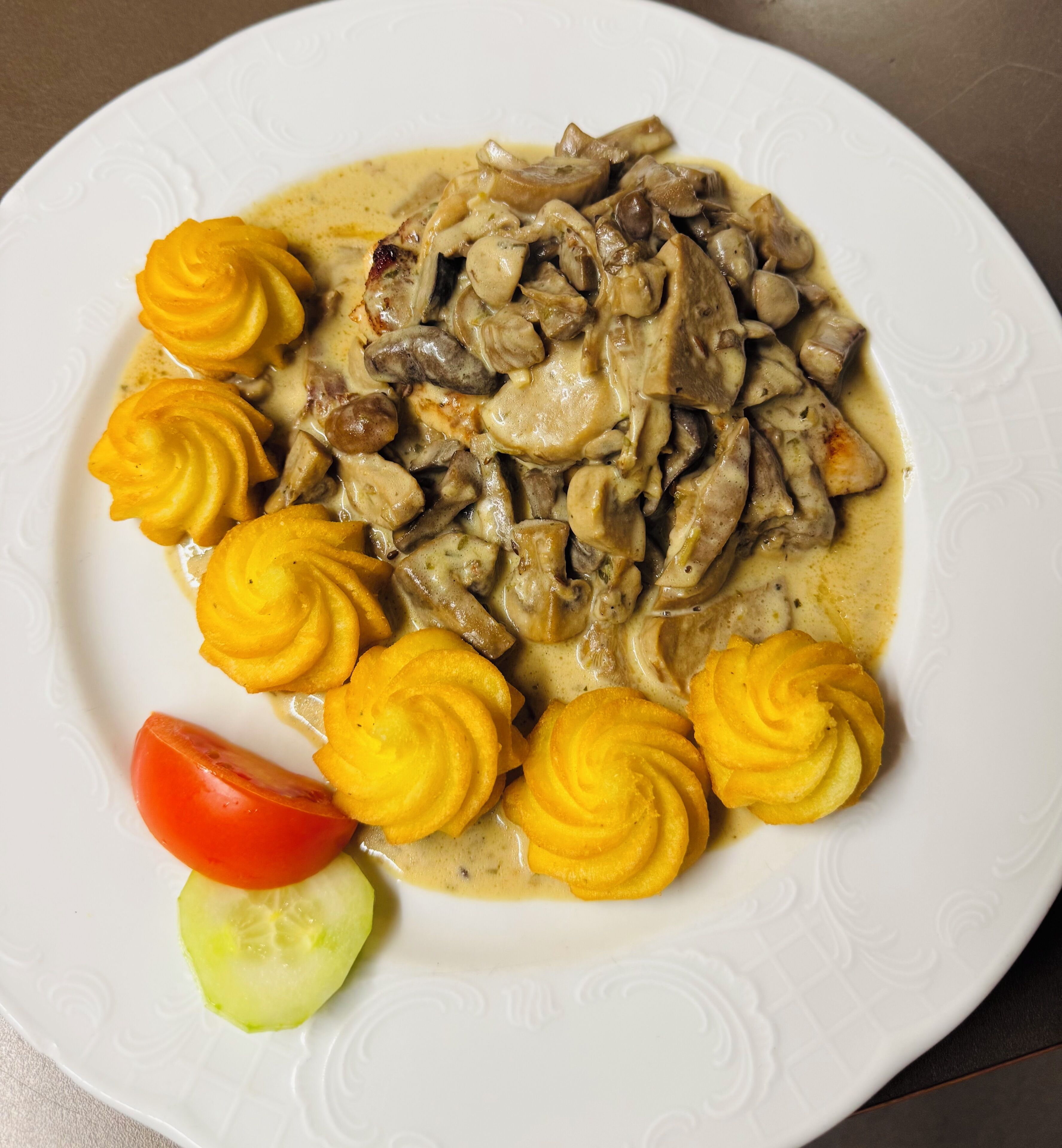 A plate of food with mushrooms and cream sauce, accompanied by a slice of tomato and a cucumber.