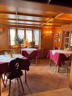A restaurant with wooden walls, multiple tables with red tablecloths, and potted plants. - Hotel-Restaurant Maien (Todtmoos)