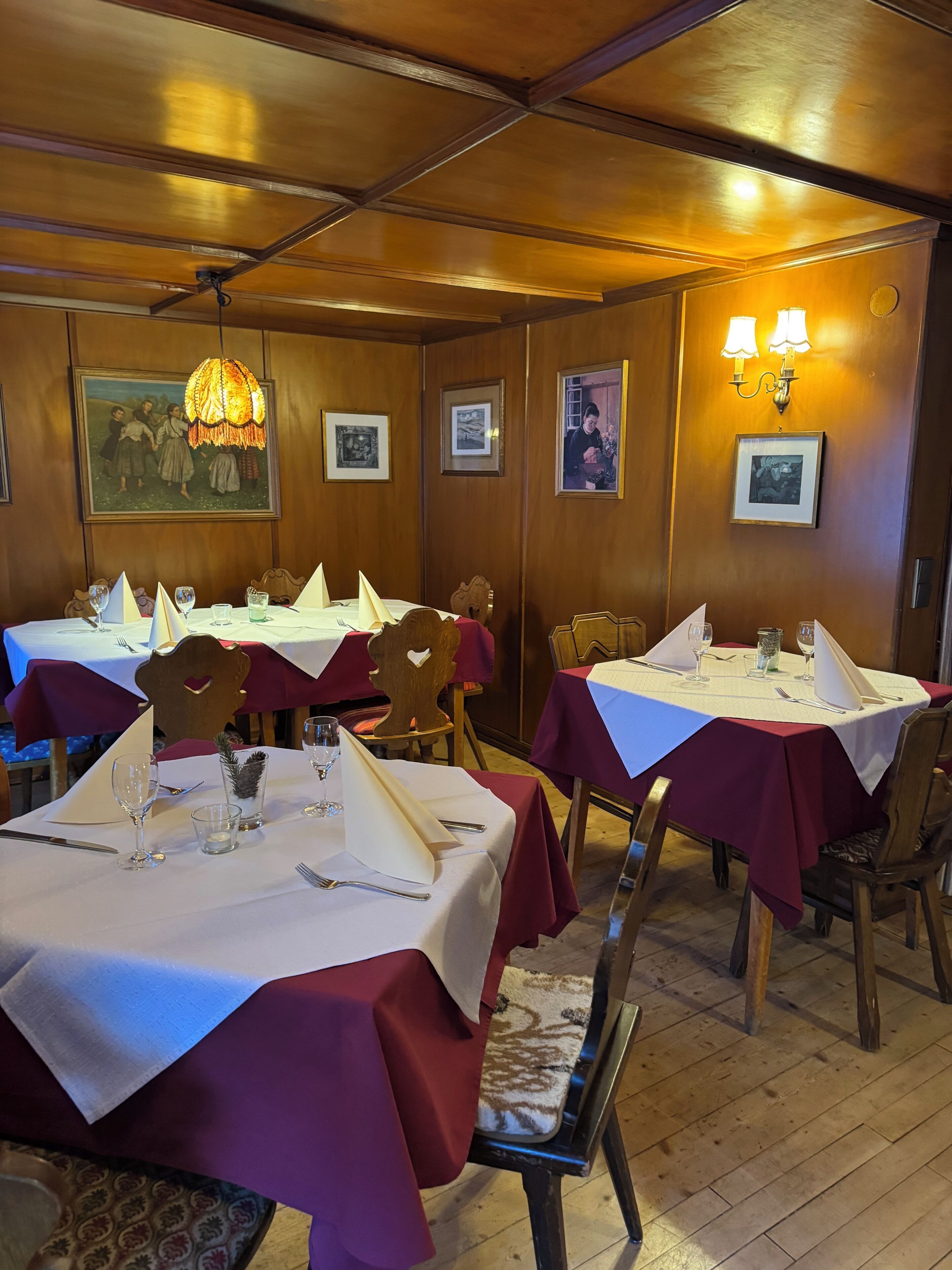 Un restaurante con paneles de madera, cuadros enmarcados en las paredes y mesas dispuestas con manteles blancos y servilletas rojas.