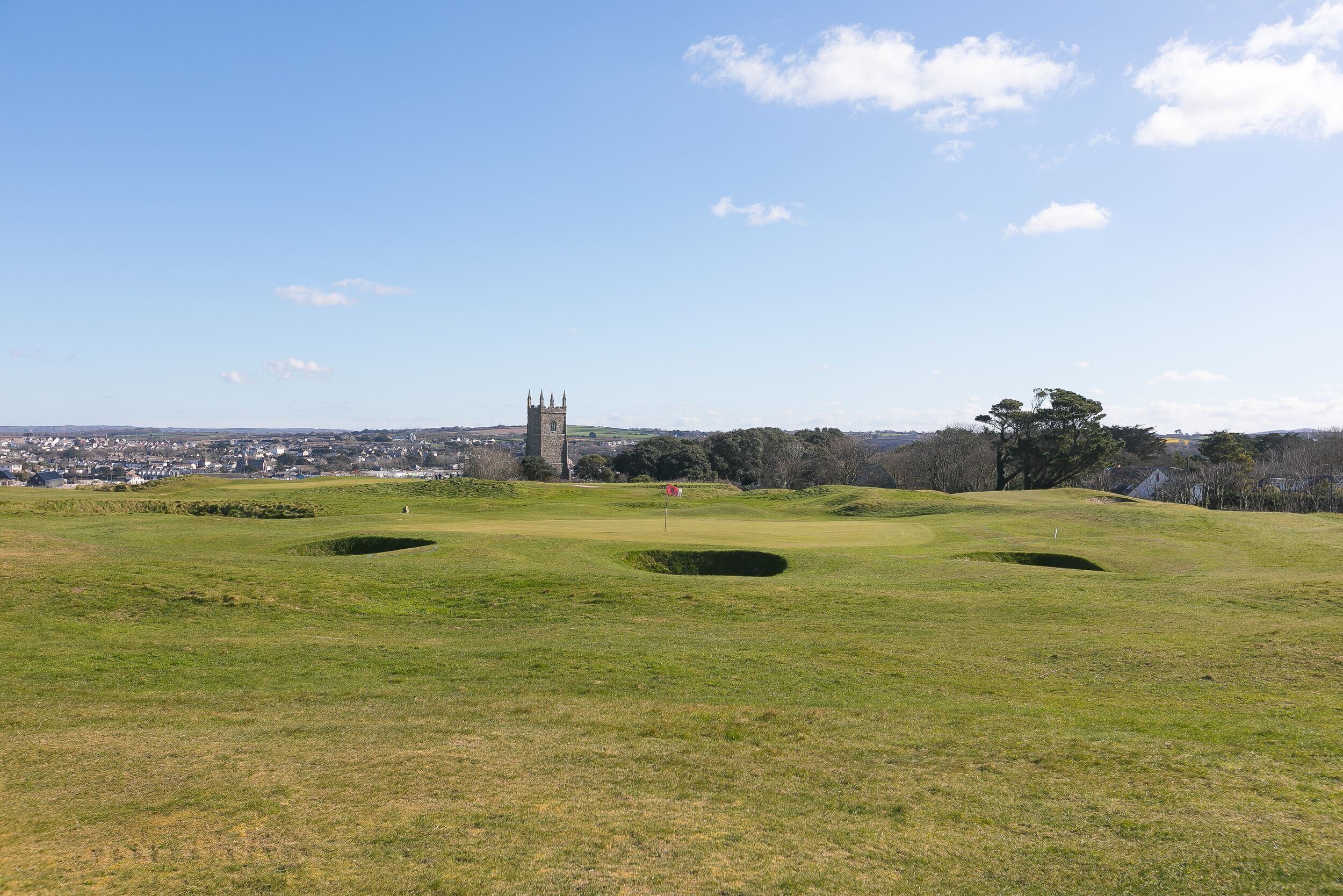 Een golfbaan met bunkers en een toren in de verte.