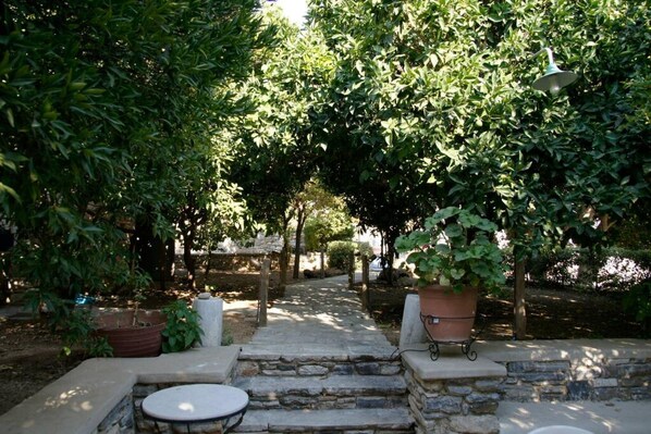 A stone pathway leading to a seating area with a table and chairs, surrounded by lush greenery and potted plants.