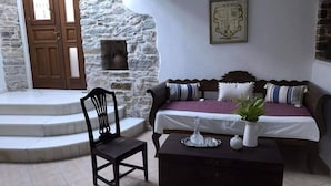 A cozy room with a stone wall, a wooden door, a bed with a purple bedspread, a wooden chair, and a small table with a plant. - Giannakis Filoxenia (Naxos)
