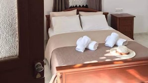 A hotel room with a wooden bed, beige bedding, a nightstand, and a window with curtains. - Giannakis Filoxenia (Naxos)